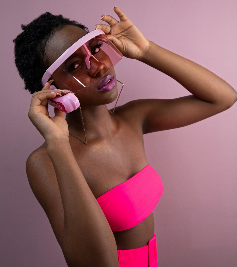 A woman with short hair wearing a neon pink tube top and futuristic pink visor sunglasses.