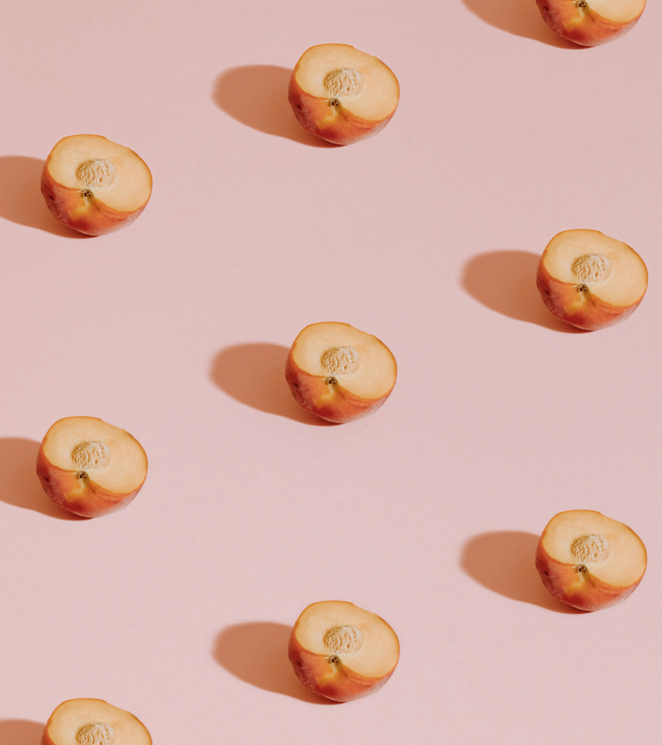 A repeating pattern of peach halves with pits facing upward on a pale pink background.