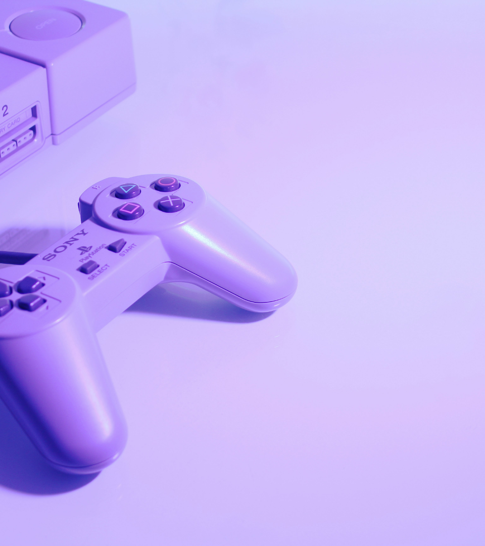 A classic PlayStation controller and console bathed in monochrome purple light.