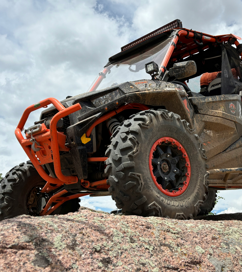 Low-angle shot of a muddy, orange and black off-road UTV parked on a rocky ridge.